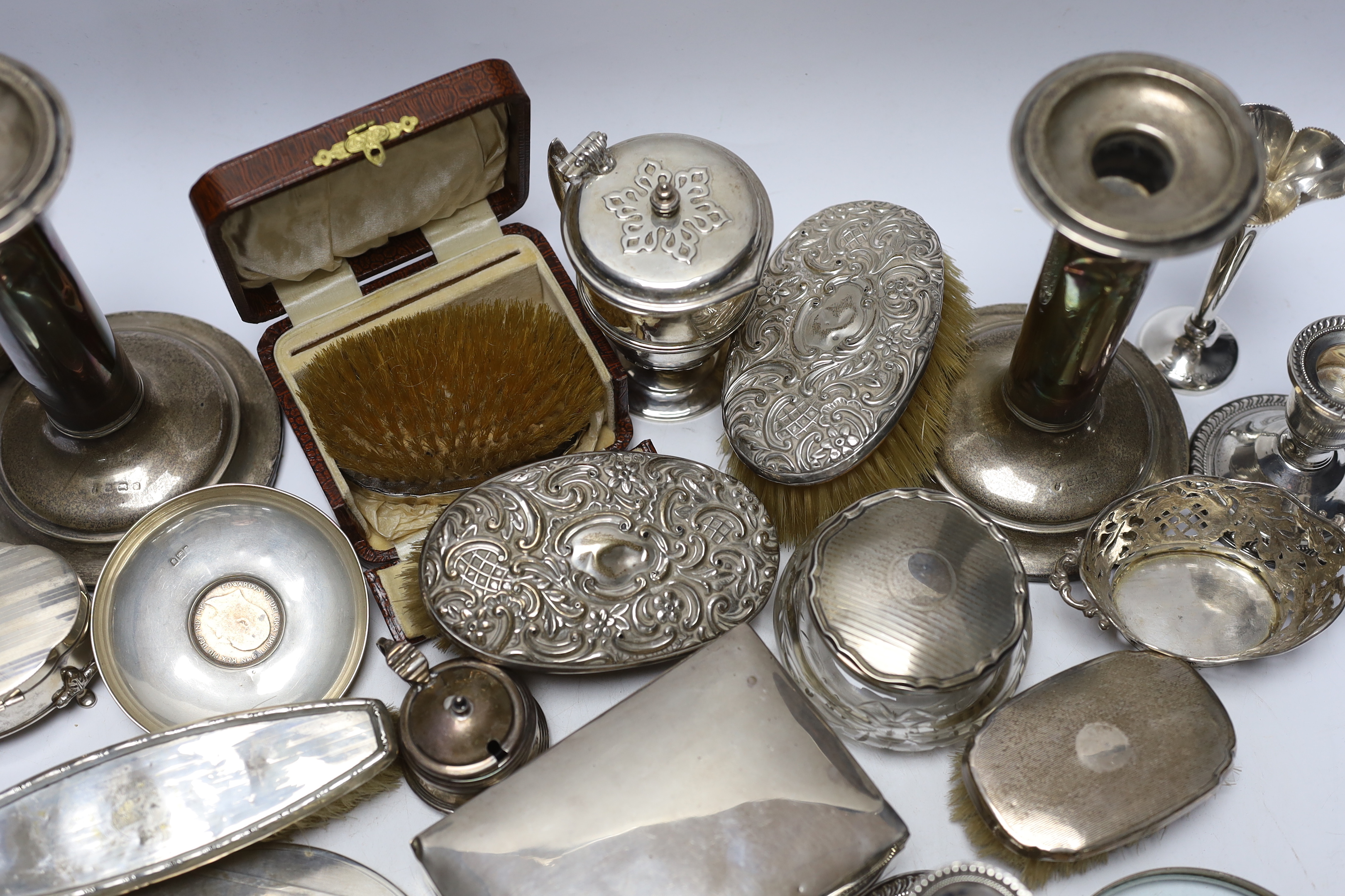 Sundry silver items including a pair of candlesticks, marks rubbed, handled magnifying glass, lidded vase, hand mirror, five brushes, cigarette box, trinket box, toilet jar and eleven other items including a novelty shoe